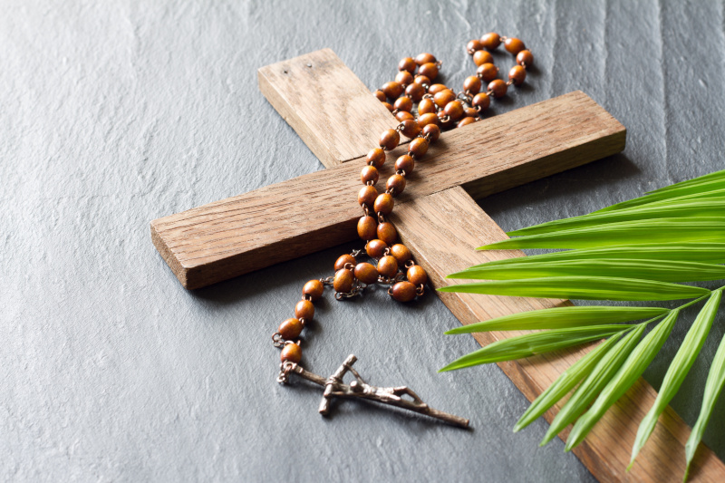 Ein Holzkreuz, eine Kette mit Jesus am Kreuz und ein Palmblatt